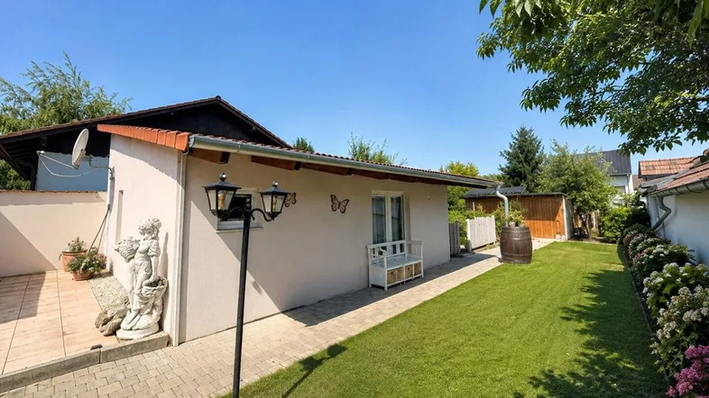 Gepflegter Gartenbereich mit Rasenfläche, kleiner Terrasse und dekorativer Außenbeleuchtung am Haus.