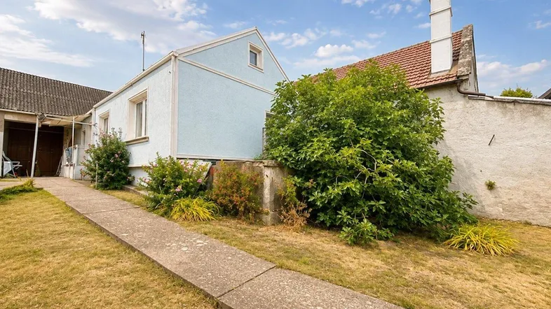 Außenansicht des Hauses mit hellblauer Fassade, Gartenbereich und einem Betonweg.