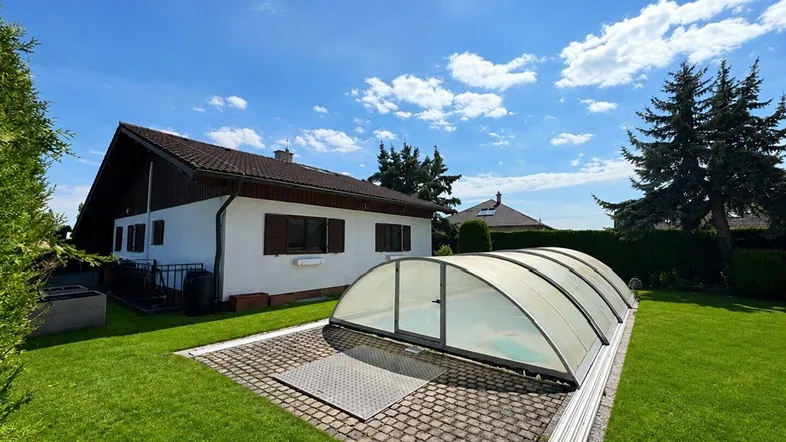 Großer grüner Garten mit Einfamilienhaus und überdachtem Swimmingpool unter blauem Himmel.