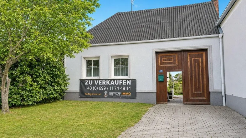Vorderansicht eines Hauses mit gepflegtem Rasen, gepflasterter Auffahrt und einem "Zu Verkaufen"-Schild.