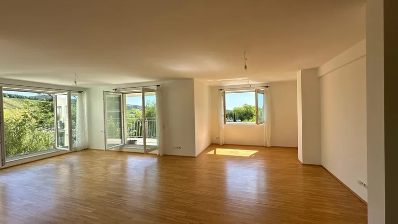 Helles und geräumiges Wohnzimmer mit Parkettboden, großen Fenstern und Zugang zum Balkon.