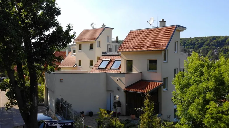 Mehrere moderne Gebäude mit hellen Fassaden und roten Ziegeldächern in einer grünen Umgebung.