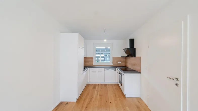 Helle Küche mit weißen Schränken, Holzrückwand und Parkettboden, bereit für die Installation von Geräten.