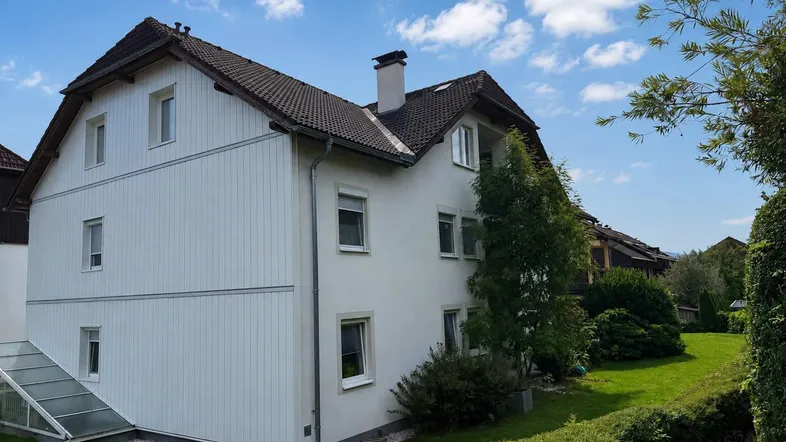 Gepflegtes Wohnhaus mit weißer Fassade, Satteldach und einem grünen Gartenbereich mit Hecken.
