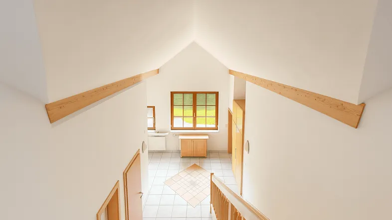 Heller Flurbereich mit hohen Decken, Holztreppe und Blick auf die Landschaft durch das Fenster.