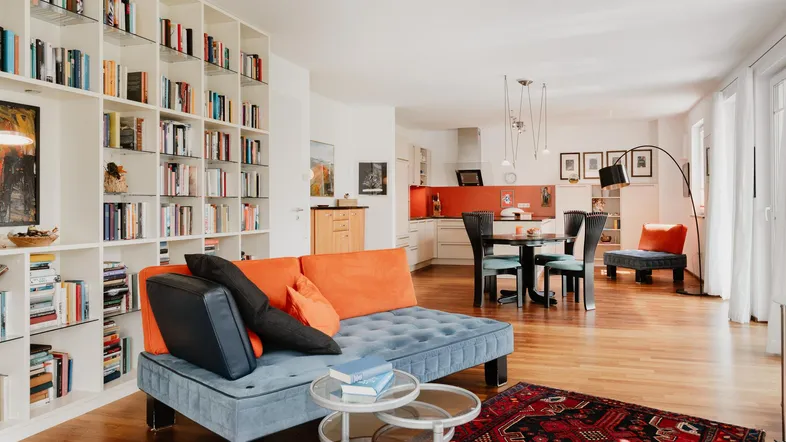 Heller offener Wohn- und Essbereich mit großem Bücherregal, Sofa und integrierter Küche.