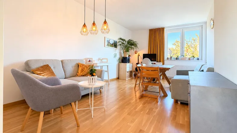 Helles und offenes Wohnzimmer mit Essbereich, Parkettboden und Blick ins Grüne durch große Fenster.