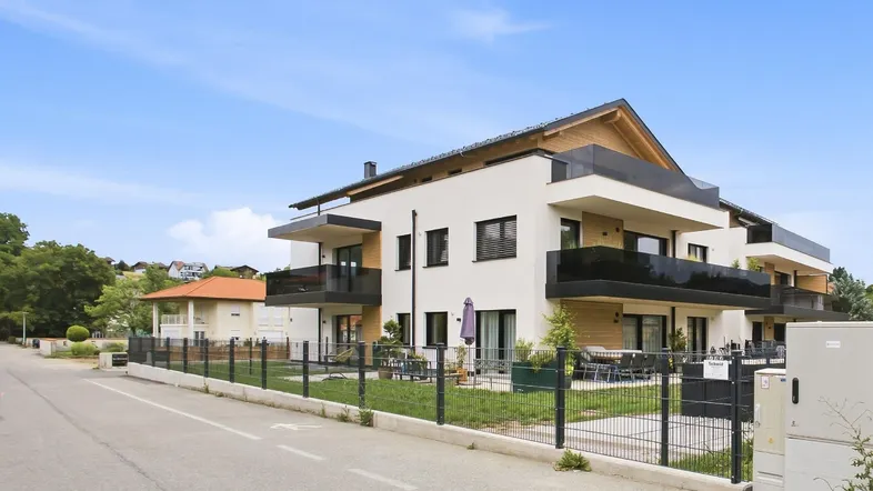 Modernes Mehrfamilienhaus mit weißer Fassade, Balkonen und gepflegtem Vorgarten in sonniger Lage.