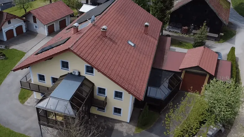 Luftaufnahme eines Einfamilienhauses mit rotem Ziegeldach, Wintergarten und Photovoltaikanlage in ländlicher Umgebung.