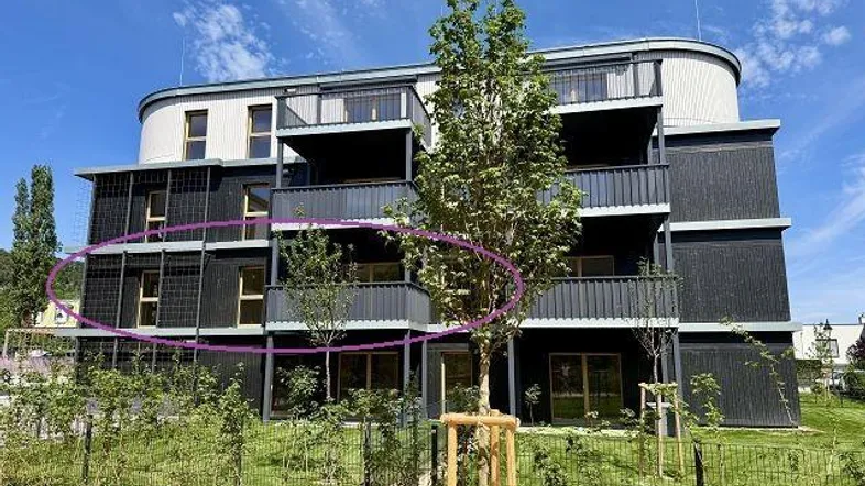 Modernes Mehrfamilienhaus mit dunkler Fassade, mehreren Balkonen und neu angelegtem Gartenbereich.