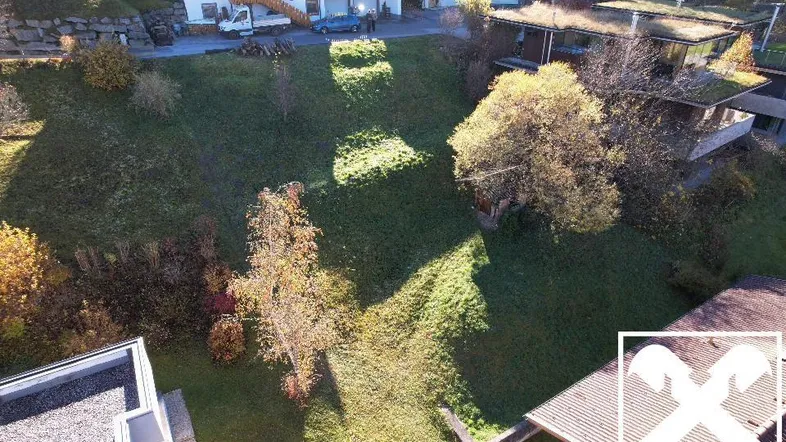 Luftaufnahme eines grünen Grundstücks mit umliegenden Häusern und herbstlicher Vegetation.