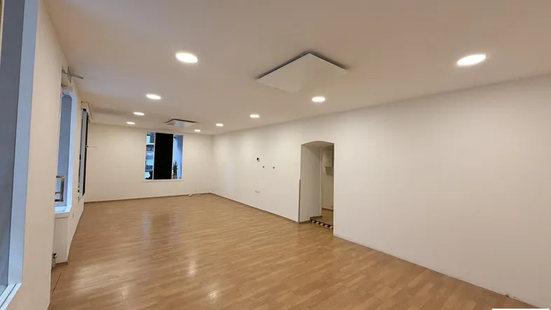 Geräumiger, leerer Geschäftsraum mit hellem Laminatboden und Einbaustrahlern an der Decke.