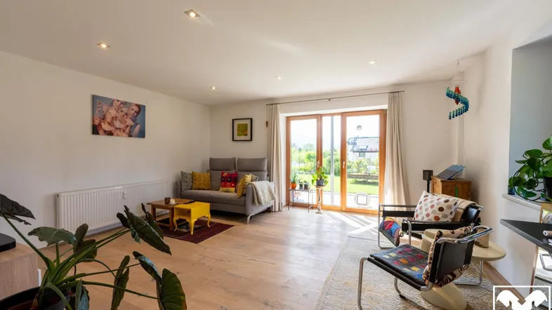 Helles Wohnzimmer mit Holzboden, großen Fenstern und Zugang zum Garten.