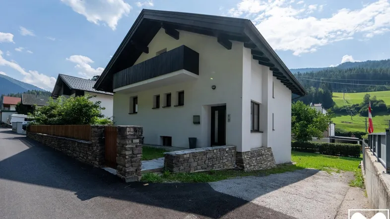 Modernes Einfamilienhaus mit weißer Fassade, schwarzem Dach und kleinem Vorgarten.