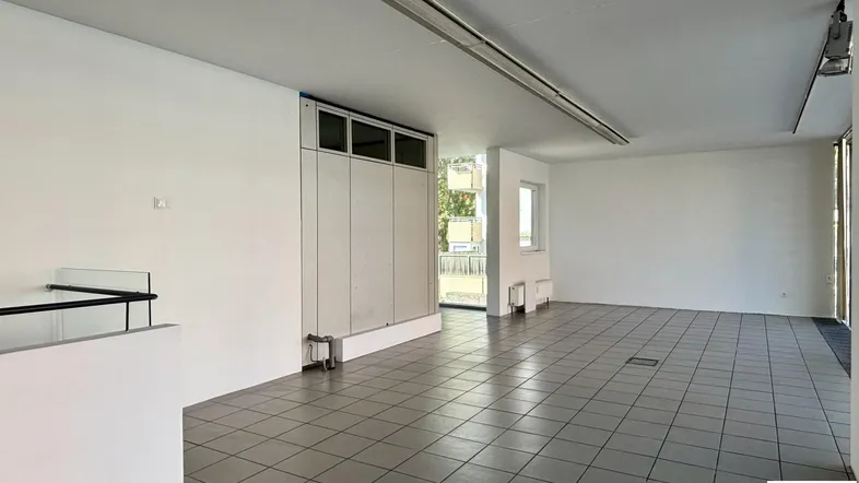 Geräumiger, leerer Gewerberaum mit hellen Fliesenböden, weißen Wänden und viel Tageslicht.