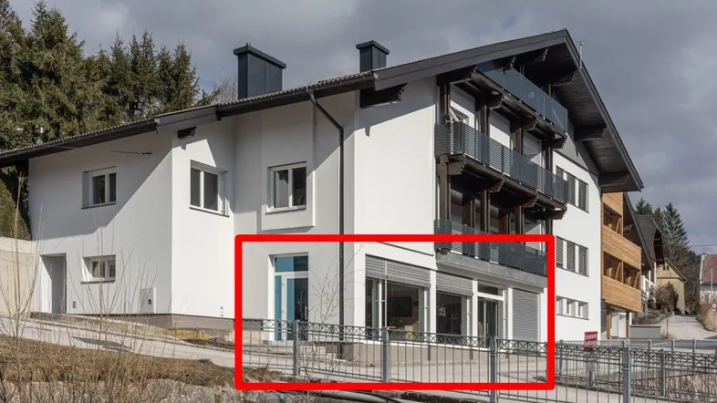 Modernes Gebäude mit weißer Fassade, großen Fenstern und Balkonen, umgeben von Bäumen.