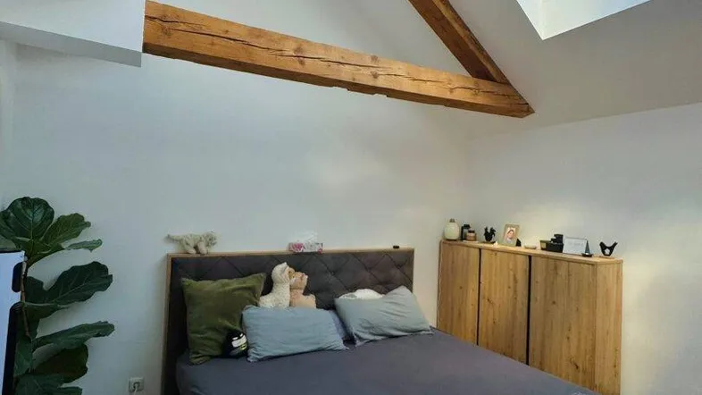 Gemütliches Schlafzimmer im Dachgeschoss mit sichtbaren Holzbalken und einem großen Dachfenster für viel Tageslicht.