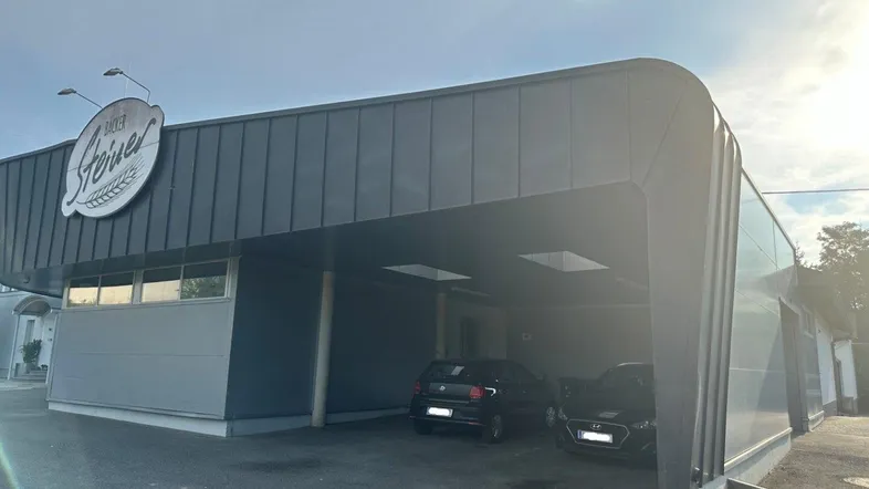 Modernes Geschäftsgebäude mit integriertem Carport und Parkplätzen unter einem geschwungenen Dach.