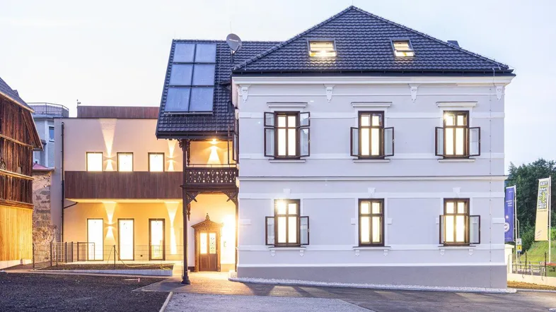 Historisches Gebäude mit moderner Erweiterung und Solaranlage bei Dämmerung, gut gepflegt.