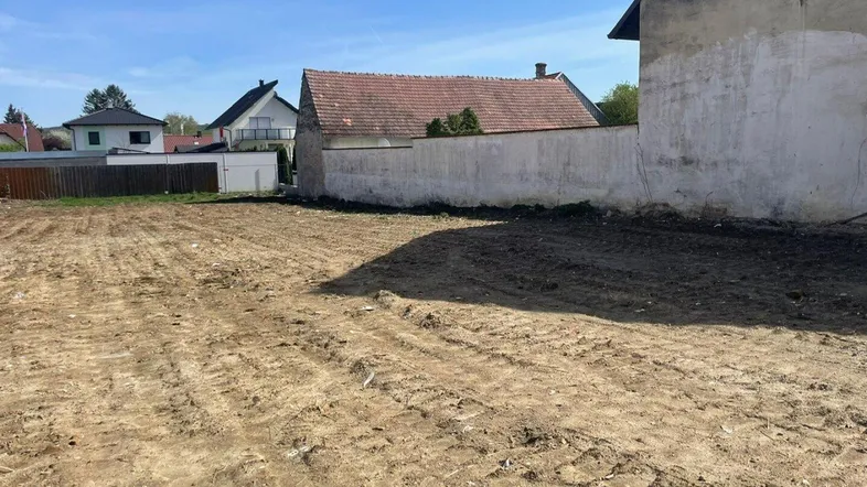 Freies Baugrundstück mit vorbereitetem Boden für zukünftige Bebauung und umgebenden Häusern.