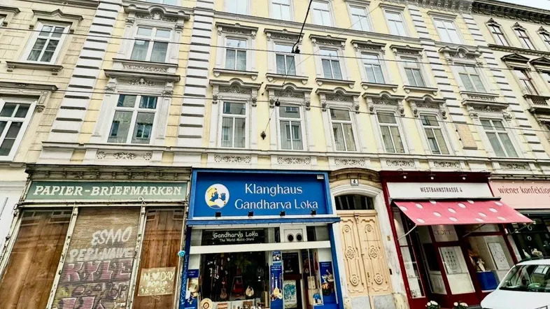 Klassisches Wiener Wohnhaus mit gelber Fassade und Geschäften im Erdgeschoss an einer belebten Straße.