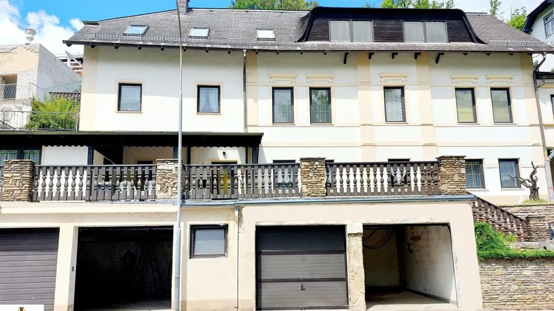 Mehrfamilienhaus mit Garagen im Erdgeschoss und Balkon im ersten Stock.
