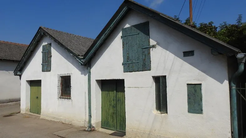 Weiß verputztes Gebäude mit grünen Holztüren und Fensterläden unter blauem Himmel.