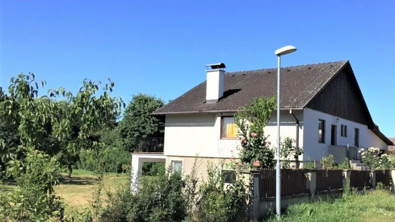 Freistehendes Einfamilienhaus mit Satteldach und großem Gartenbereich unter blauem Himmel.