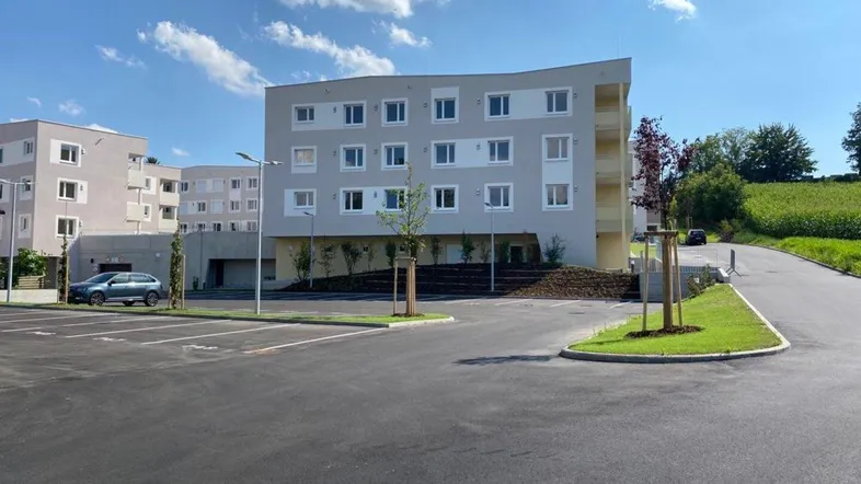 Modernes Mehrfamilienhaus mit Parkplätzen und grüner Umgebung unter blauem Himmel.