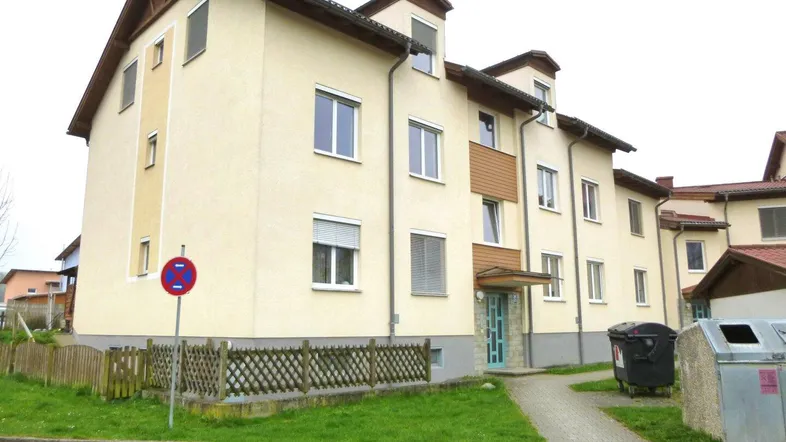 Mehrfamilienhaus mit heller Fassade, Satteldach und gepflegter Grünfläche im Vorgartenbereich.