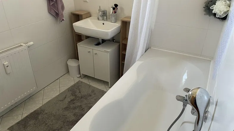 Helles Badezimmer mit Badewanne, Waschbecken und weißen Fliesen, funktional eingerichtet.