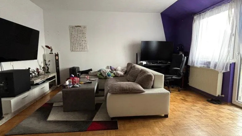 Gemütliches Wohnzimmer mit Parkettboden, beiger Couch und einer auffälligen lila Akzentwand.