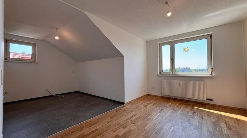 Helles Zimmer im Dachgeschoss mit Holzboden und schrägen Wänden, bietet vielseitige Nutzungsmöglichkeiten.