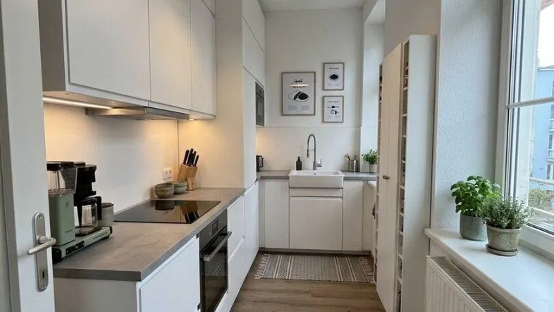 Moderne, helle Küche mit weißen Schränken, Holzarbeitsplatte und Laminatboden.