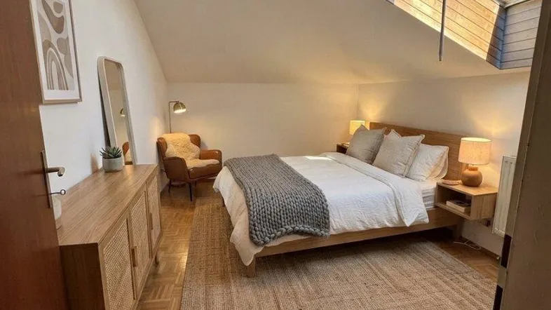 Helles Schlafzimmer im Dachgeschoss mit Holzboden, gemütlicher Einrichtung und großem Dachfenster.