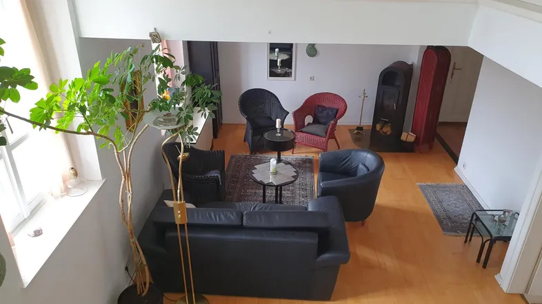 Geräumiges Wohnzimmer mit hohen Decken, Holzboden und gemütlicher Sitzecke auf zwei Ebenen.