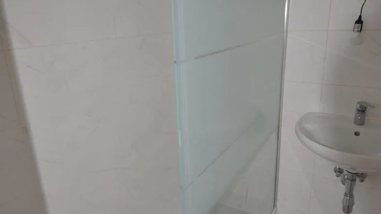 Modernes Badezimmer mit großer Duschkabine, weißen Fliesen und einem einzelnen Waschbecken.