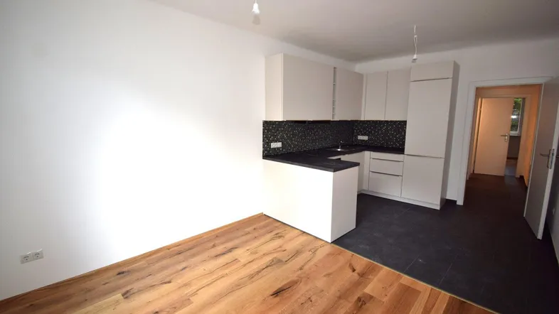 Moderne Küchenzeile mit weißen Schränken, dunklem Fliesenspiegel und Holzboden in einem offenen Bereich.