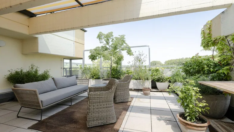 Geräumige Dachterrasse mit bequemen Loungemöbeln, Sonnenschutz und üppiger Bepflanzung für entspannte Stunden im Freien.