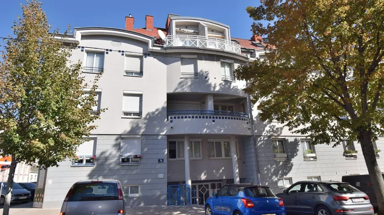 Mehrfamilienhaus mit moderner Architektur, geschwungenen Balkonen und Bäumen im Vordergrund.