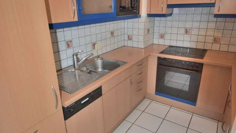 Kleine Küche mit hellbraunen Holzschränken, blauen Akzenten und weißen Fliesenboden.