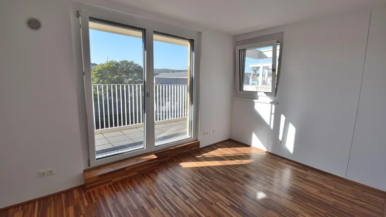Helles Zimmer mit Holzboden und Zugang zu einer großen Terrasse, ideal als Schlaf- oder Wohnbereich.
