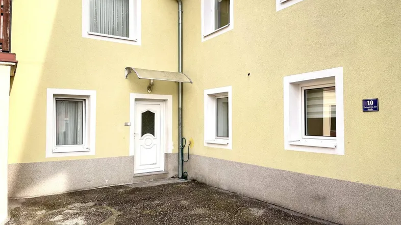 Gelbe Fassade eines Wohnhauses mit weißer Eingangstür und mehreren Fenstern.