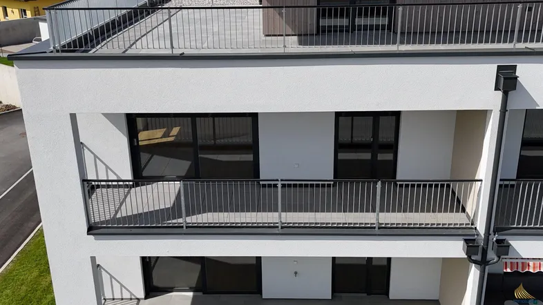 Moderne Wohnanlage mit mehreren Balkonen und einer Dachterrasse. Die Fassade ist weiß verputzt mit dunklen Geländern.
