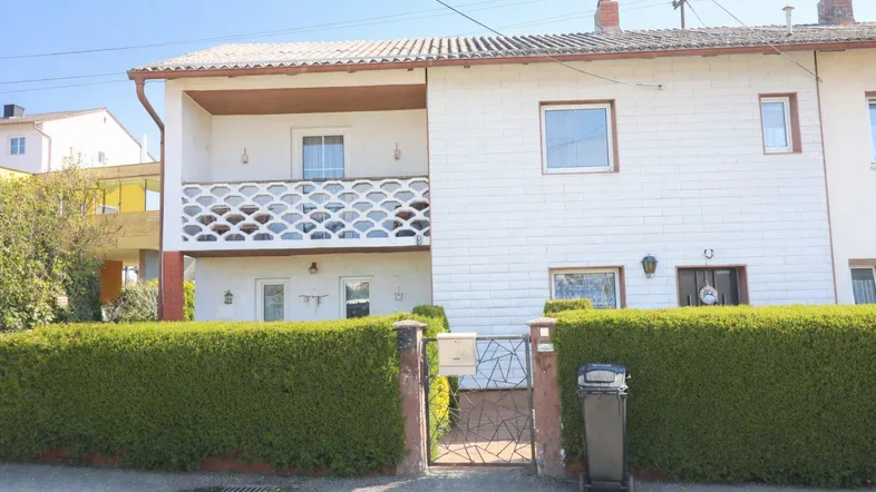 Vorderansicht eines Einfamilienhauses mit Balkon und gepflegter Hecke im Vorgarten.