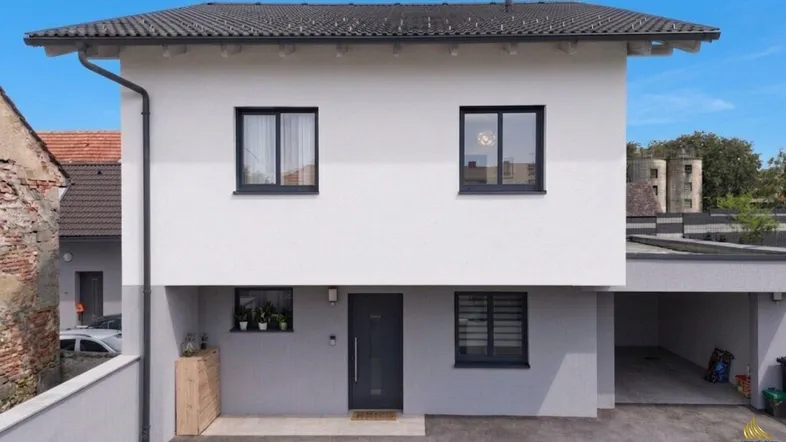 Modernes Einfamilienhaus mit weißer Fassade, dunklem Dach und integriertem Carport.