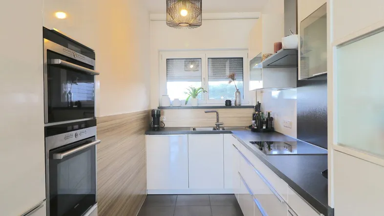 Moderne Küche mit weißen Hochglanzfronten, integrierten Geräten und Fenster für natürliches Licht.