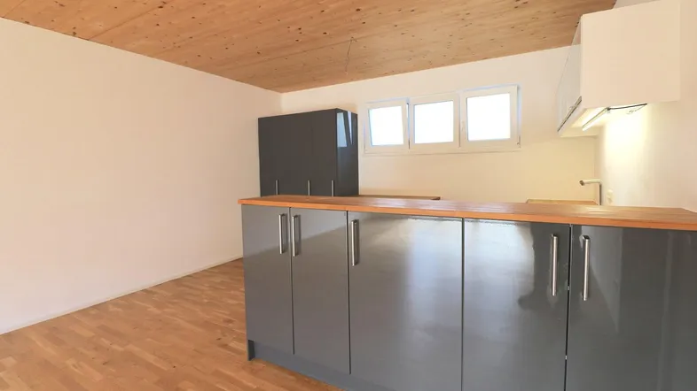 Moderne Küche mit grauen Schränken, Holzarbeitsplatte und Holzdecke, bereit für die Installation von Geräten.