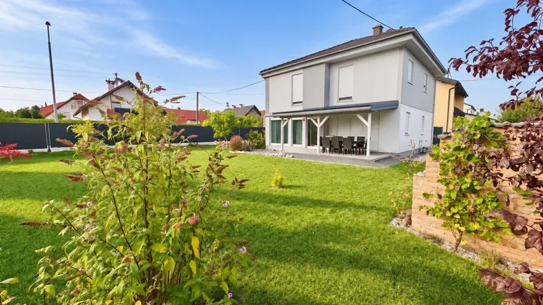 Großer gepflegter Garten mit weitläufiger Rasenfläche und überdachtem Terrassenbereich am Haus.