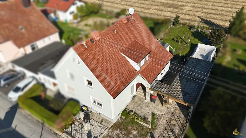 Luftaufnahme eines Einfamilienhauses mit rotem Ziegeldach, Carport und angrenzendem Garten.